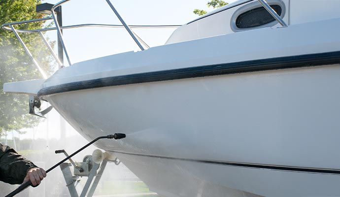 A person is pressure washing the hull of a boat
