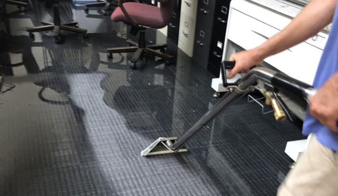 Technician cleaning commercial office carpet with a cleaning wand.