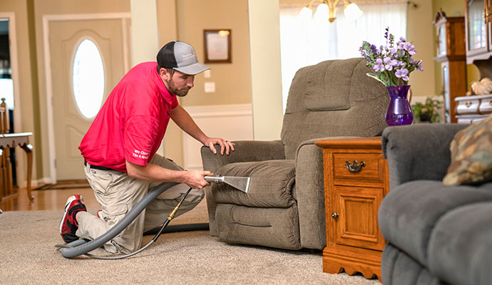 Technician cleaning an upholstered armchair with a steam extraction tool.