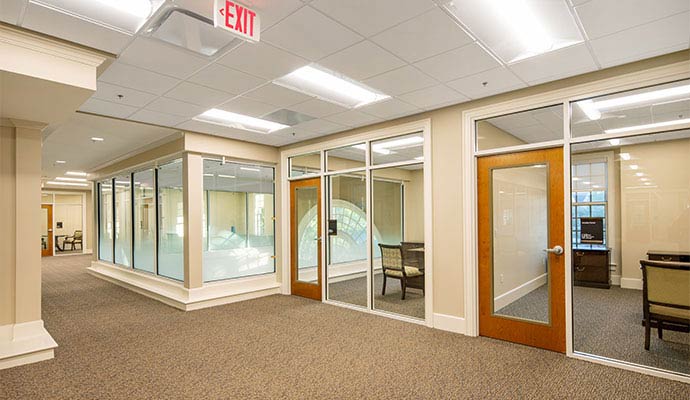 Clean commercial office hallway with glass meeting rooms, carpet flooring and professional interior design