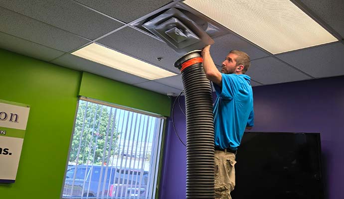Technician connecting commercial negative air vacuum hose to ceiling air duct vent