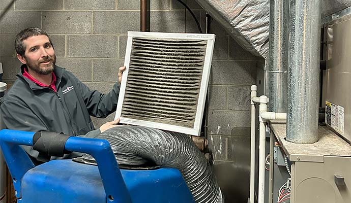 Technician displaying a dirty, dust-clogged HVAC air filter during duct inspection