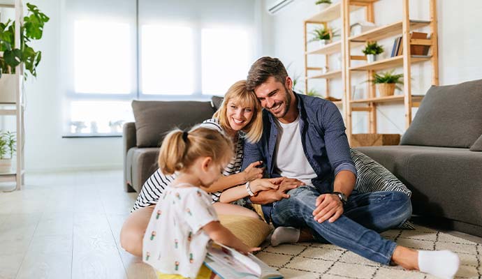 Family with young child sitting and reading together in a clean living room