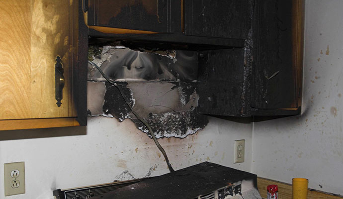 Charred kitchen cabinets and drywall with heavy soot damage after a fire.