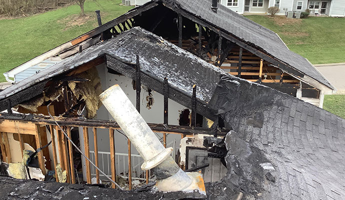 Severe structural fire damage with burned roof trusses and wall framing.