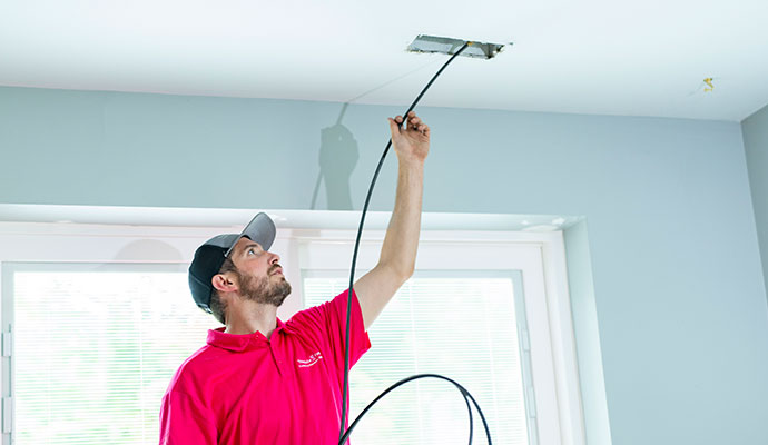 Technician cleaning a ceiling air duct with a flexible cable.