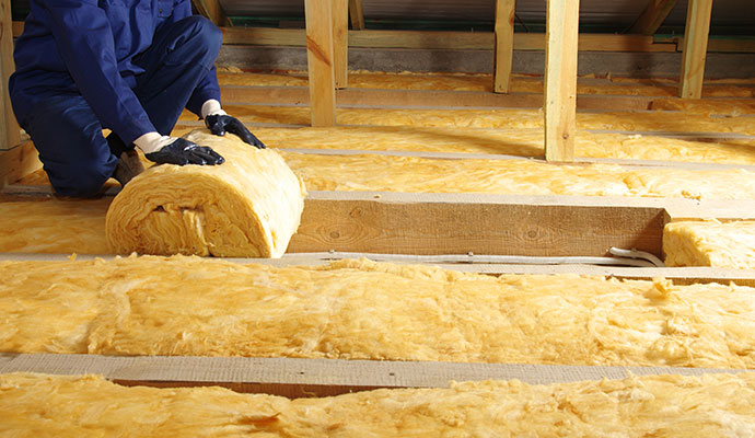 Worker installing new fiberglass insulation in a residential attic.