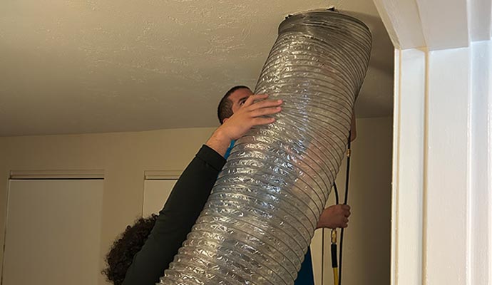 Two experts holding a large flexible air duct during cleaning