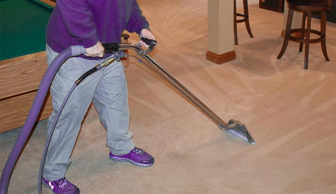 A professional cleaner using a hot water extraction tool to clean a beige carpet in a room with a pool table