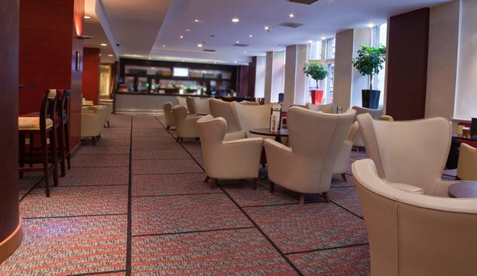 Spacious hotel lounge featuring cream wingback chairs and patterned red and grey commercial carpeting