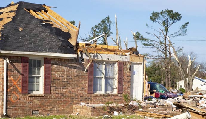 Residential home with severe hurricane damage missing roof sections debris and destroyed surrounding trees