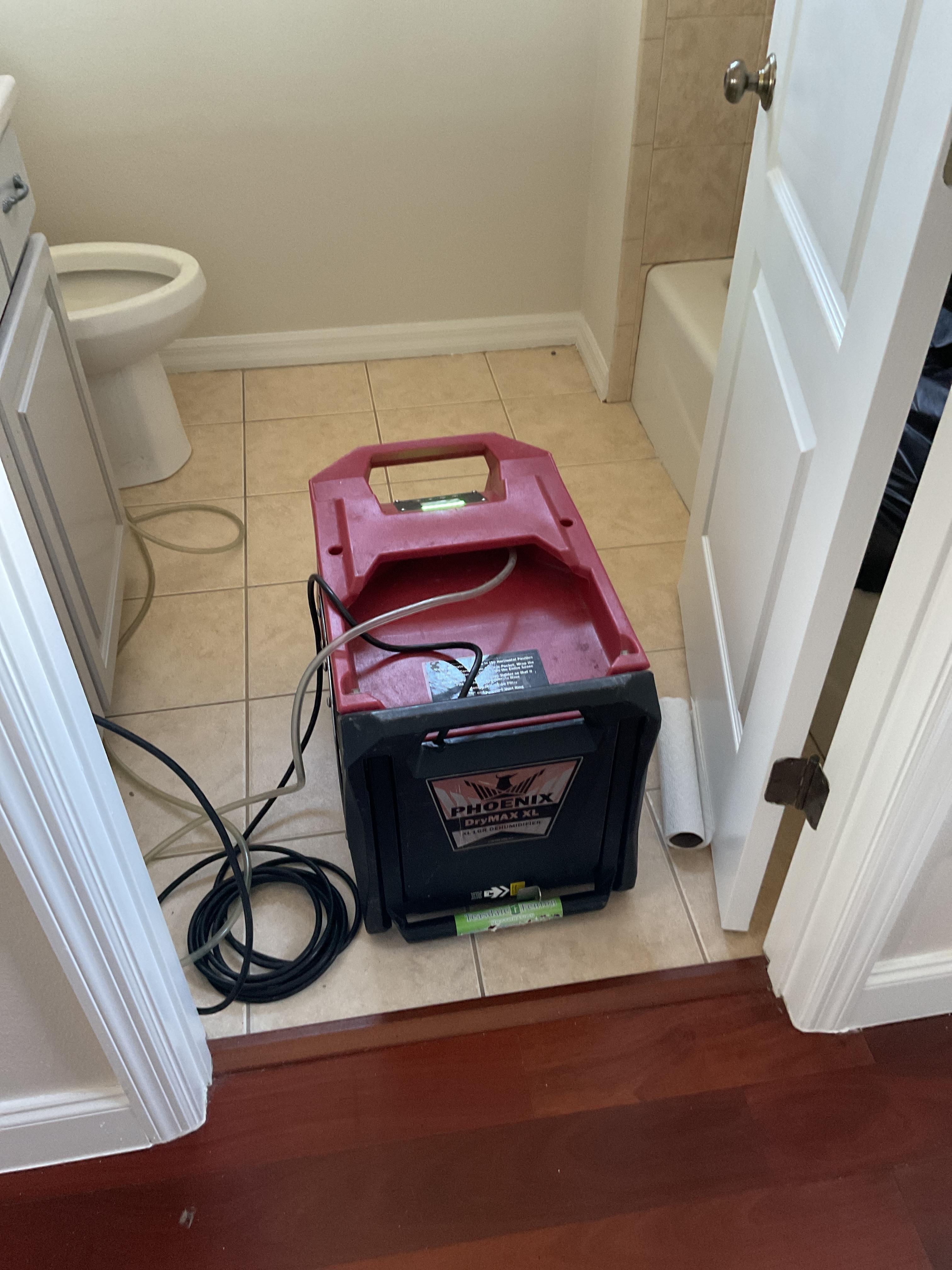 A view looking into the affected bathroom showing a red and black Phoenix DryMAX XL industrial LGR dehumidifier stationed on the tiled floor.