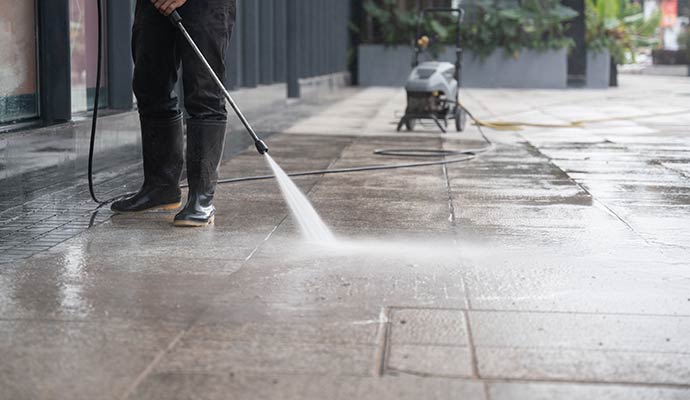 Worker using pressure washer to clean outdoor concrete surface and remove dirt from pavement area