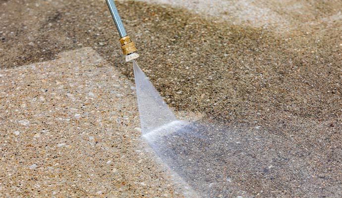 High pressure water wand cleaning a dirty concrete surface showing a clear before and after difference