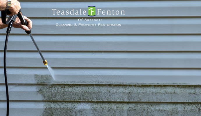 A person is pressure washing the dirty siding of a house.