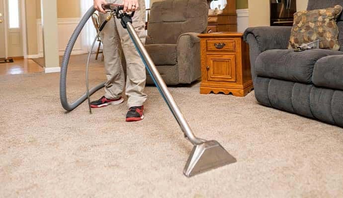 Technician using a professional steam cleaning wand on residential carpet in a living room