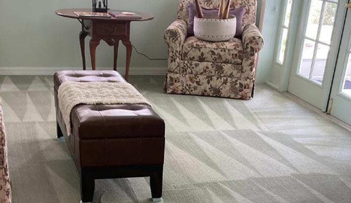 Living room area featuring a brown leather ottoman and floral armchair on top of a freshly cleaned light green patterned carpet