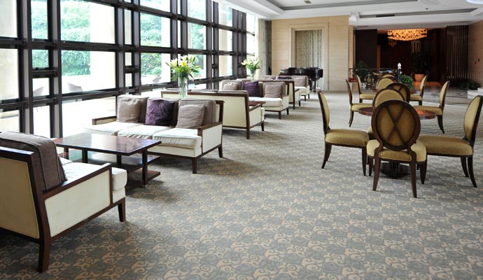 Large hotel lobby or restaurant seating area with patterned grey commercial carpet and white sofas by floor-to-ceiling windows