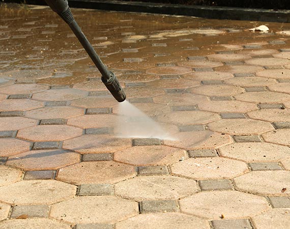 A professional cleans a residential or commercial walkway with a high-powered pressure washing tool