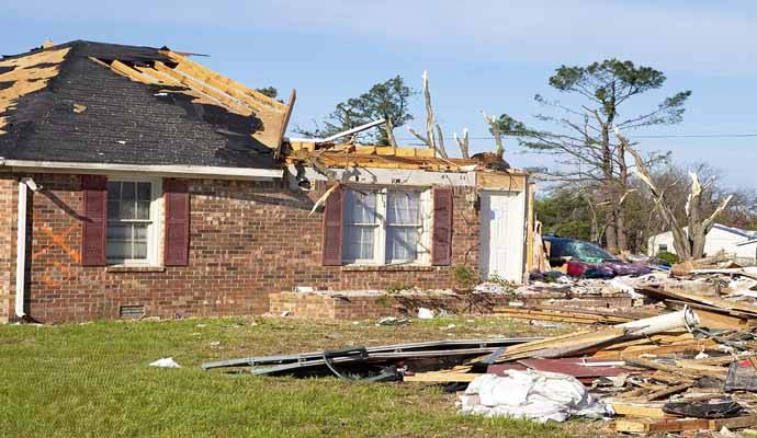 Residential home with severe storm damage missing roof sections debris and destroyed surrounding trees