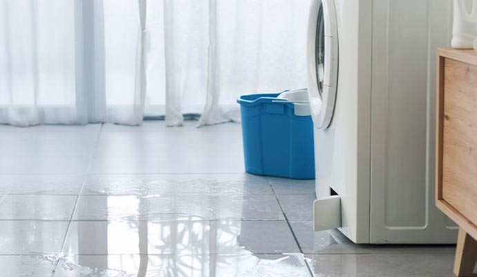 Water leaking from a washing machine onto a tiled floor.